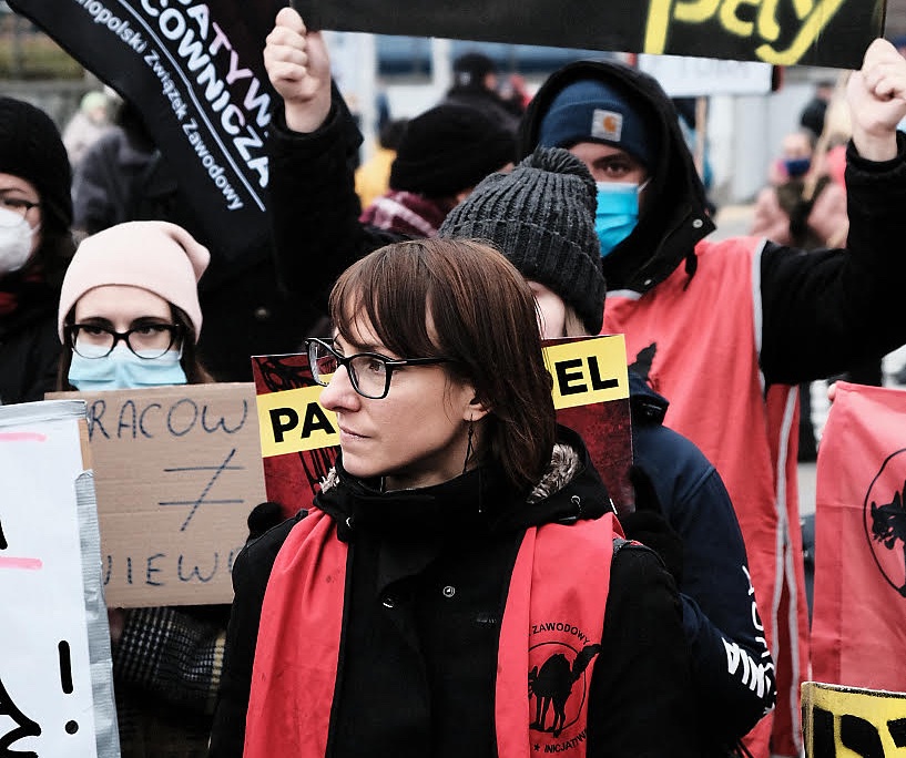 Magda, with glasses and a red vest with a wildcat cat icon on it, stands with fellow Amazon workers and Inicjatywa Pracownicza union members